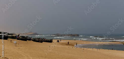 Fishing boats, fishermen and gulls on a beach near Oualidia, Morocco.
