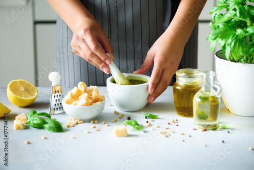 Woman hands making italian pesto in bowl. Ingredients - basil, lemon, parmesan, pine nuts, garlic, olive oil and salt on rustic wooden background. Top view, flat lay, copyspace