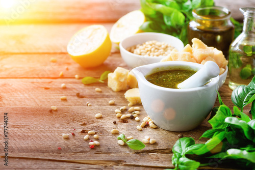 Ingredients for homemade pesto - basil, lemon, parmesan, pine nuts, garlic, olive oil and salt on rustic wooden background. Top view, flat lay, copyspace. Sunny morning