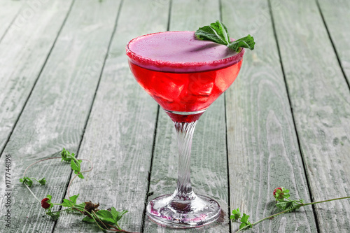 Frozen glass of alcoholic cocktail made of raspberry, mint, martini, vodka and ice. Alcoholic drink on a rustic wooden table.