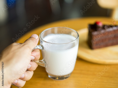 Hand holding glass of milk with chocolate cakes on top red cherry background in wooden plate on wood table