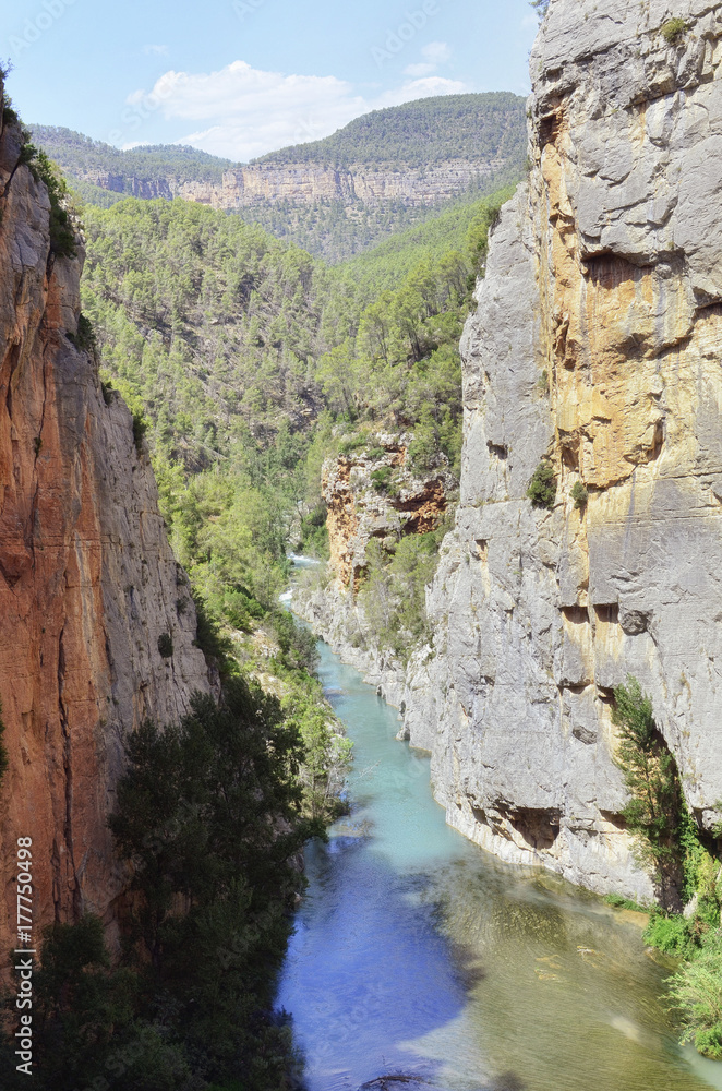 Summertime scene of Mijares river between mountains of limestone rocks, in Montanejos (Castellon - Spain). Beautiful turquoise blue waters. Natural landscape. Sunny day with some clouds.