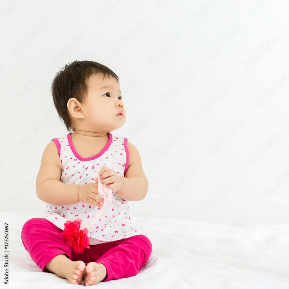 Portrait of adorable baby sitting on a white floor and holding head band Portrait of adorable baby sitting on a white floor and holding head band