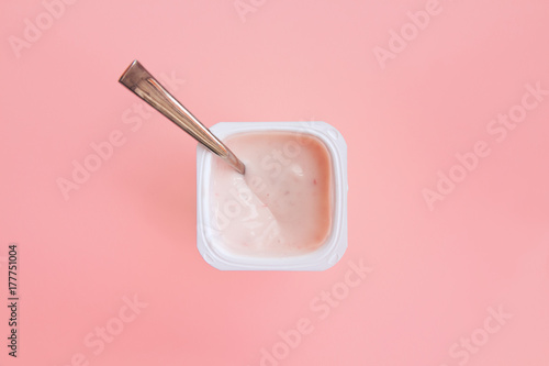 Delicious strawberry yogurt or pudding  in white plastic cup on pink background with copy space. Strawberry pink yoghurt with spoon in it. Minimal style. Flat lay, top view.