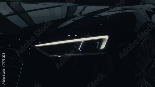 The headlights of a brand new black car blink once. Close up. photo