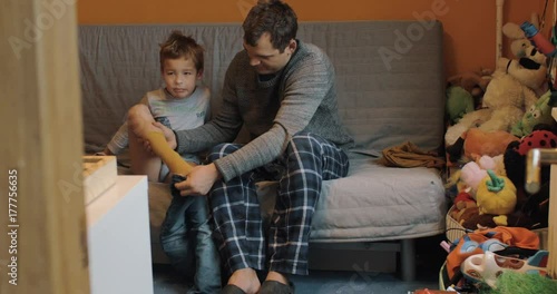 Father getting his son dressed in jeans while kid attracted to the TV
