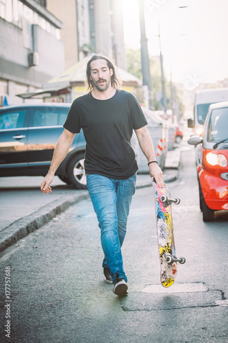 Pro skateboard rider walk down the street holding skatebord photo