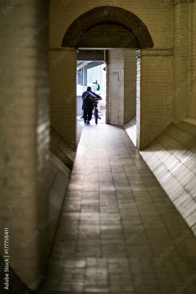 Person walking a bicycle at the end of a narrow corridor near Thames river in London England