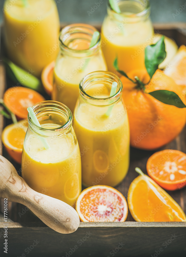 Healthy yellow smoothie with citrus fruit and ginger in bottles in wooden box over grey background, selective focus. Clean eating, vegan, dieting, weight loss, vegetarian food concept Healthy yellow smoothie with citrus fruit and ginger in bottles in wooden box over grey background, selective focus. Clean eating, vegan, dieting, weight loss, vegetarian food concept