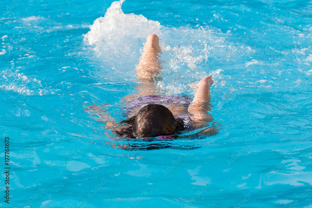 A kid in the pool, having fun and diving in blue water on a sunny summer day