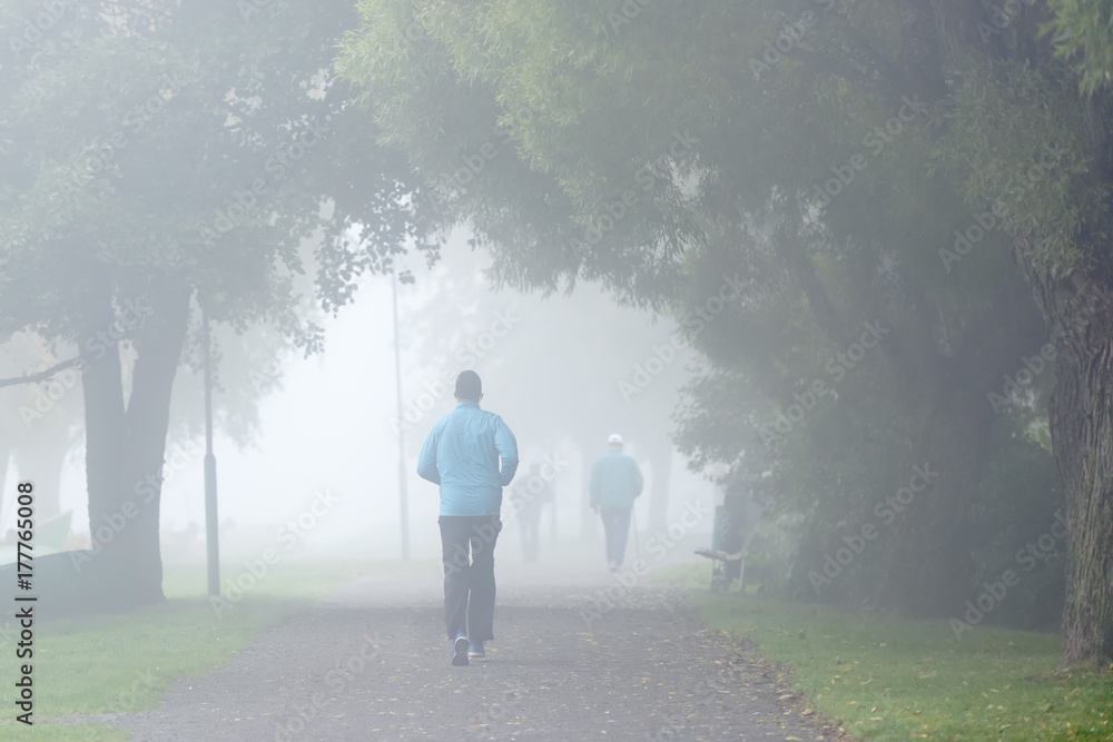 Young man jogging in park in a foggy morning