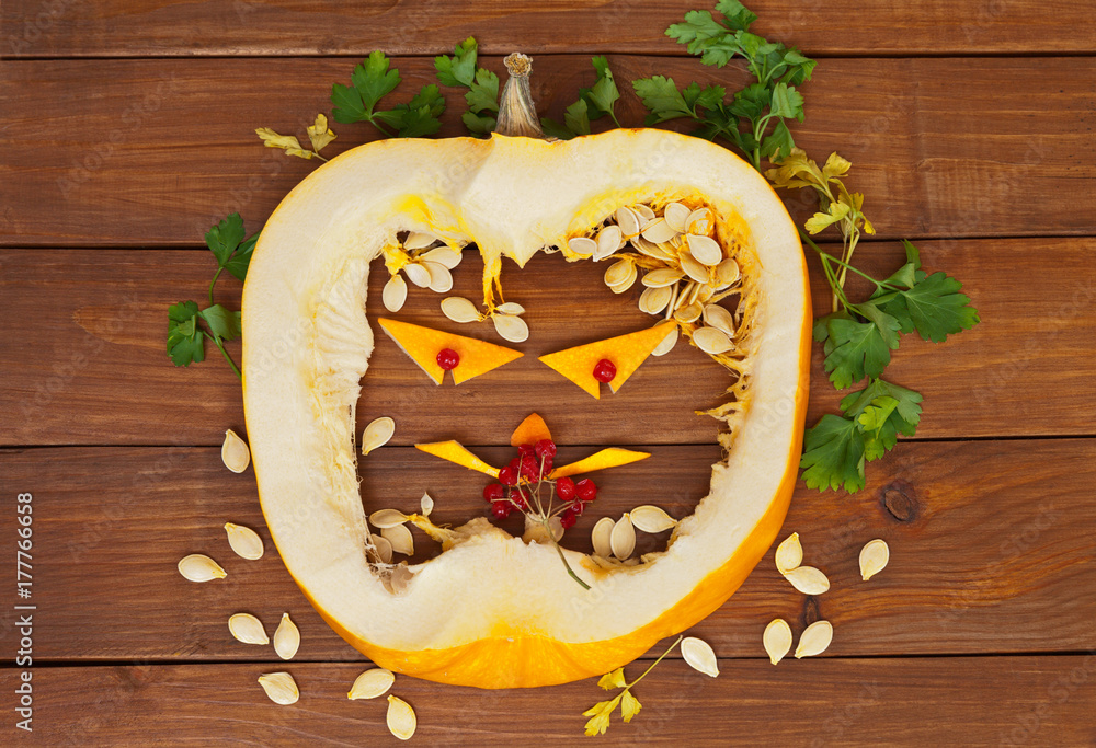 Halloween. Merry mug from a layer of pumpkin with seeds, leaves of parsley and berries of a guelder-rose on a wooden background Halloween. Merry mug from a layer of pumpkin with seeds, leaves of parsley and berries of a guelder-rose on a wooden background