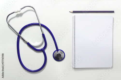 Stethoscope on a white table of the doctor's office, next to a note book and a pencil. Empty copy space for Editor's content. Top view. photo