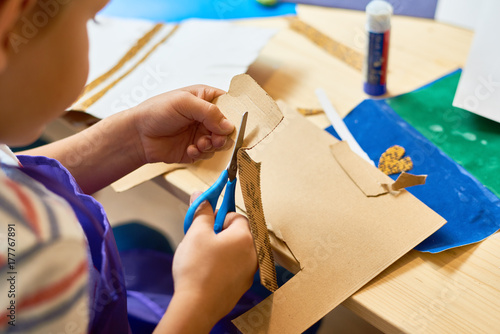 High angle portrait of unrecognizable little boy cutting paper in arts and crafts class of pre-school making handmade gift