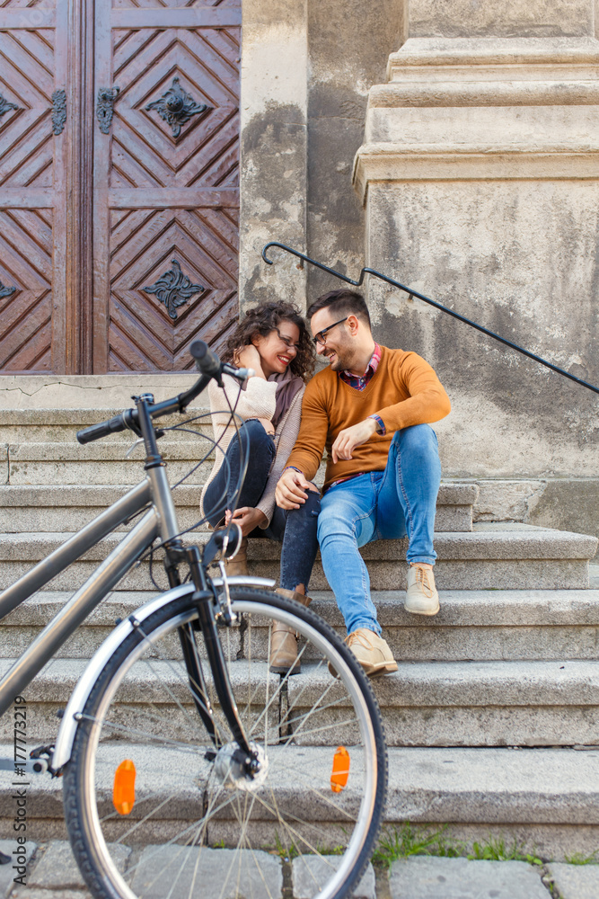 Young couple with bicycle siting on stairs in the city.