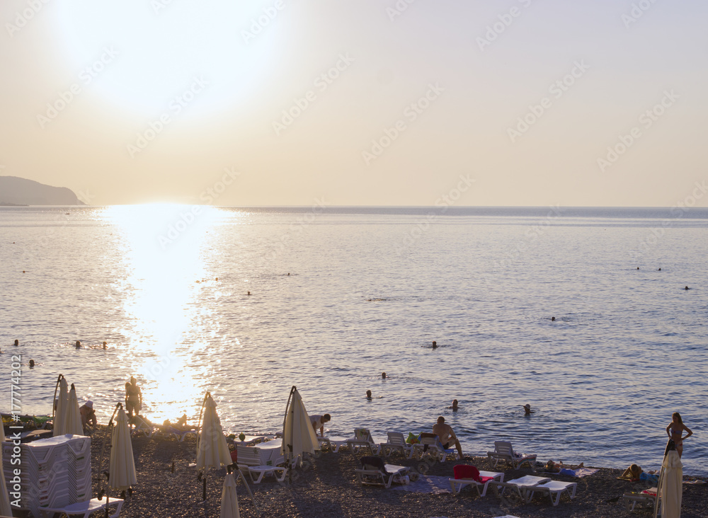 bright sunrise on the seashore, tourists can be seen and the rays of the sun