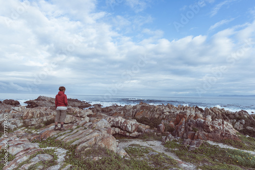 Tourist looking with binocular on the rocky coast line at De Kelders, South Africa, famous for whale watching. Winter season, cloudy and dramatic sky, toned image. photo