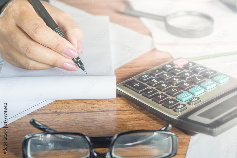 business owner doing their monthly accounting with the bills and calculator in the foreground business owner doing their monthly accounting with the bills and calculator in the foreground