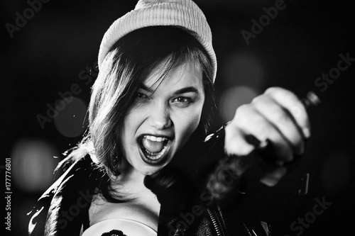 serious girl with gun on blurred background aiming at camera, screaming, monochrome