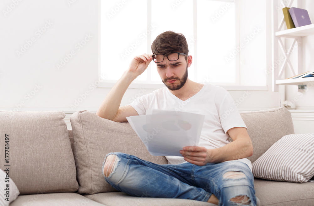 Young tired businessman reading report at home
