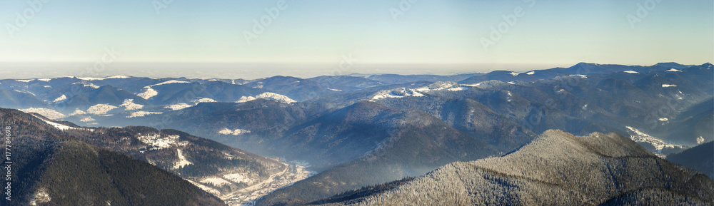 Beautiful winter panorama with fresh snow. Landscape with spruce pine trees, blue sky with sun light and high Carpathian mountains on background.