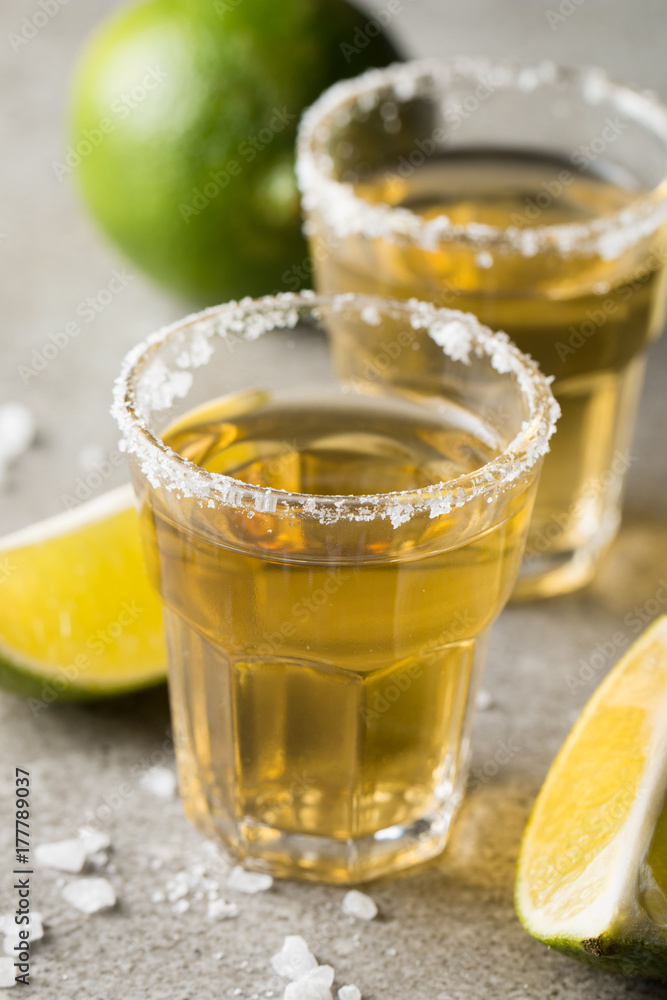 Macro focus photo of shots of golden Mexican tequila with lime and salt on wooden background. Alcoholic drink concept.