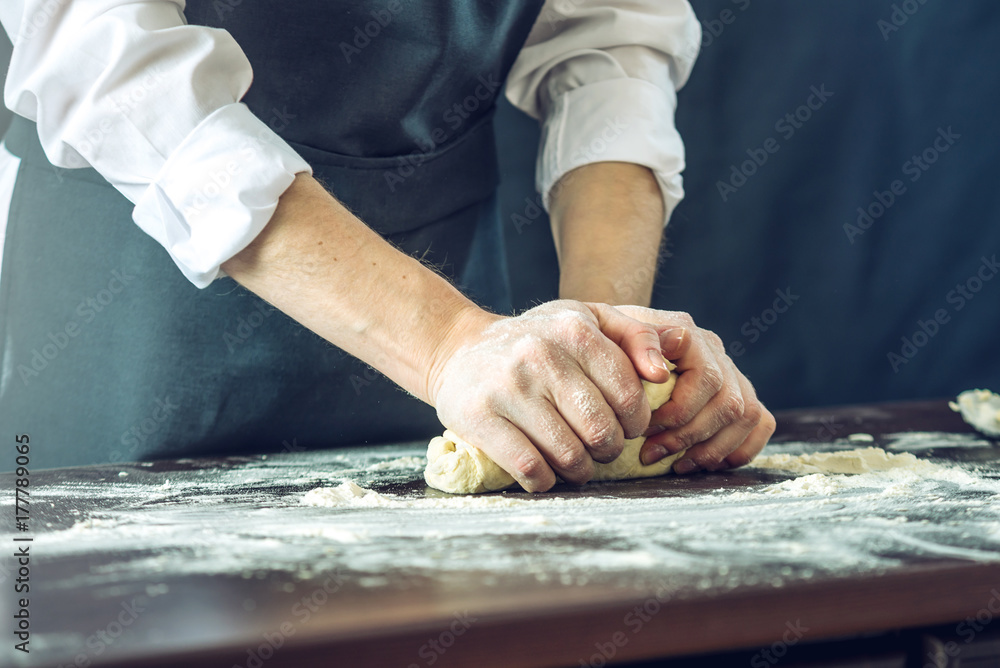The chef in black apron makes pizza dough with your hands on the table The chef in black apron makes pizza dough with your hands on the table