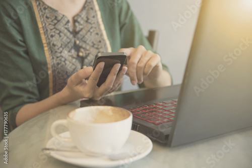 freelance business woman using smartphone at table in cafe and computer notebook with cup of coffee.