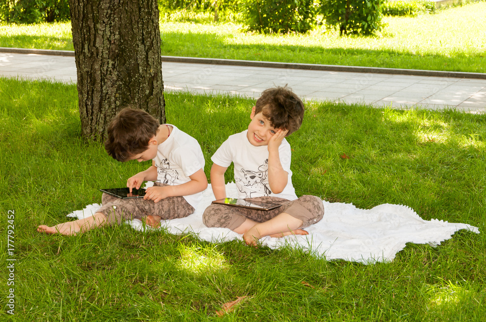 twins boys with tablets on the grass in the park twins boys with tablets on the grass in the park