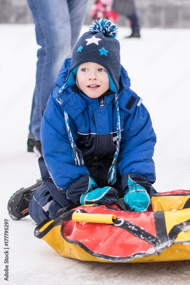 Happy boy toboggan from a snow slide on colorful tube
