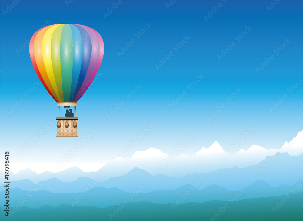 Fototapeta Uwięziony balon spokojnie dryfujący przez mglisty niebieski górski krajobraz - latający pojazd w kolorze tęczy z dwoma osobami cieszącymi się wolnością, wspaniałym widokiem i mistyczną panoramą.