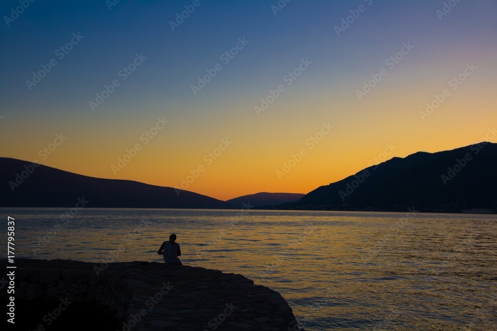 The fisherman sits by the lake at sunset. Amazing sunset between mountains and with views of the lake.