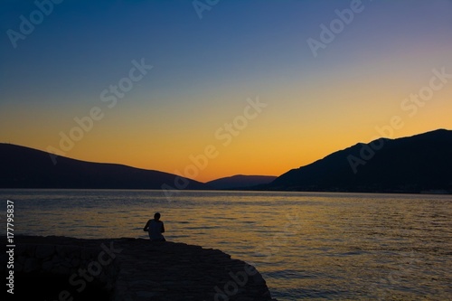 The fisherman sits by the lake at sunset. Amazing sunset between mountains and with views of the lake.