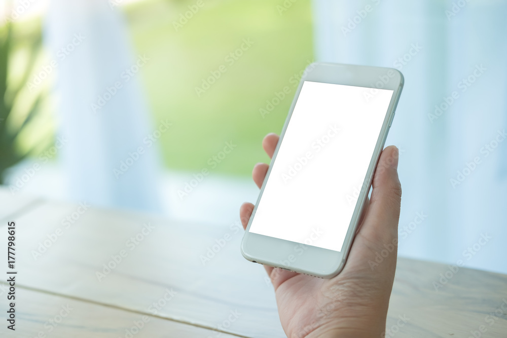 Mockup image of hand holding white mobile phone with blank screen on table in cafe