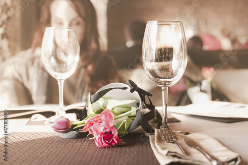 букет цветов на столике в ресторане рядом с бокалами и на фоне девушки читающей меню