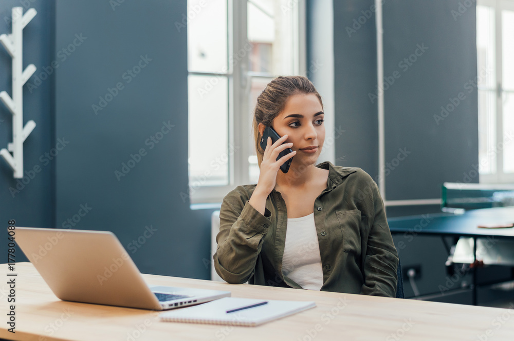 Young woman sitting in room with modern interior and talking on cellphone. Young woman sitting in room with modern interior and talking on cellphone.