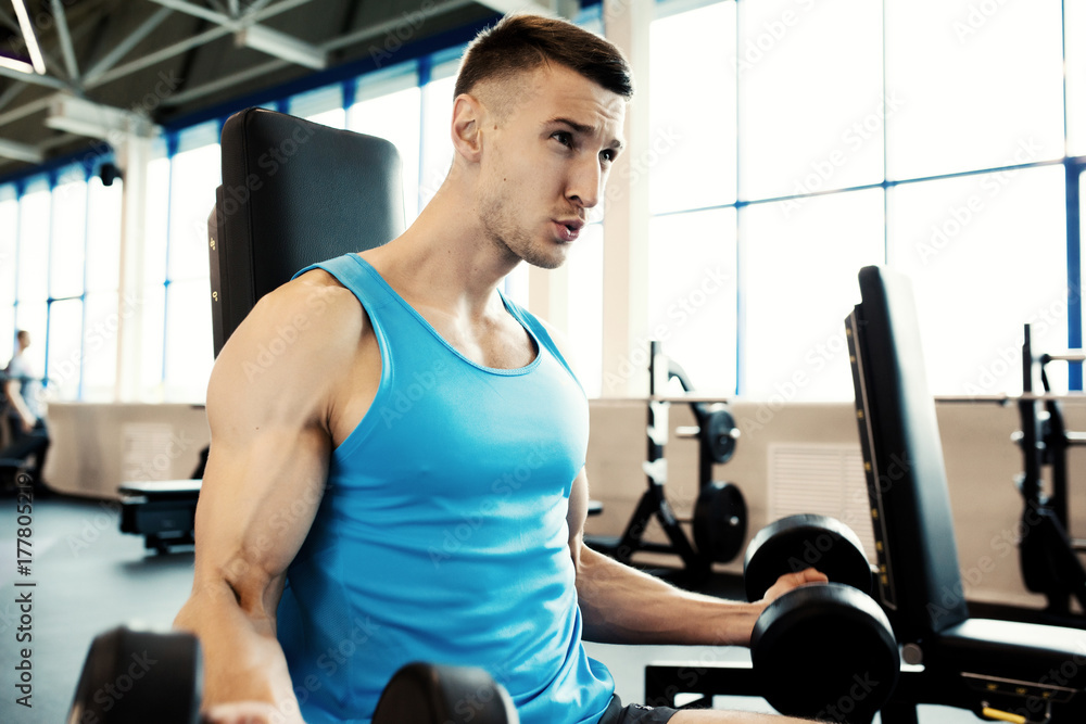 Portrait of strong man pumping arm muscles doing exercises with heavy dumbbells during workout in modern gym Portrait of strong man pumping arm muscles doing exercises with heavy dumbbells during workout in modern gym