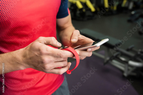 Closeup of strong male hands setting up fitness bracelet checking data on smartphone while working out in modern gym  copy space