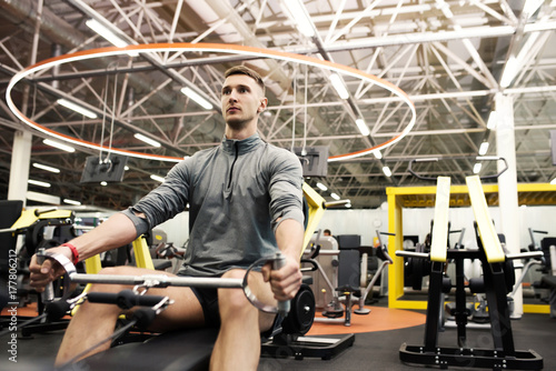 Portrait of handsome young man doing exercises using machines in modern gym in bright electric light, copy space