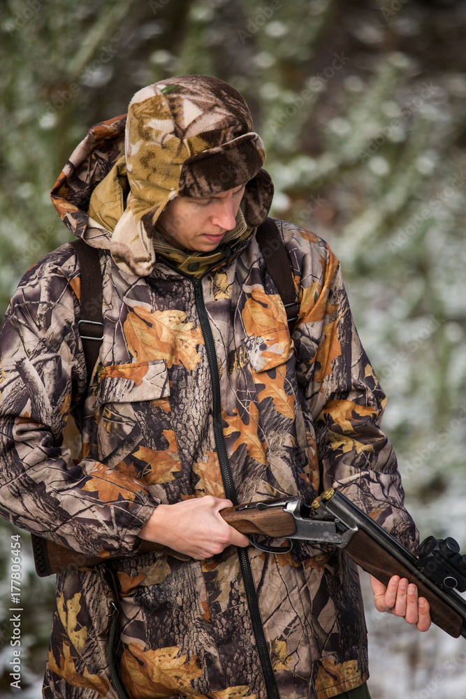 Hunter with a backpack and a hunting gun in the winter forest. Man is charging a hunting rifle. Winter snow-covered forest. Hunter with a backpack and a hunting gun in the winter forest. Man is charging a hunting rifle. Winter snow-covered forest.