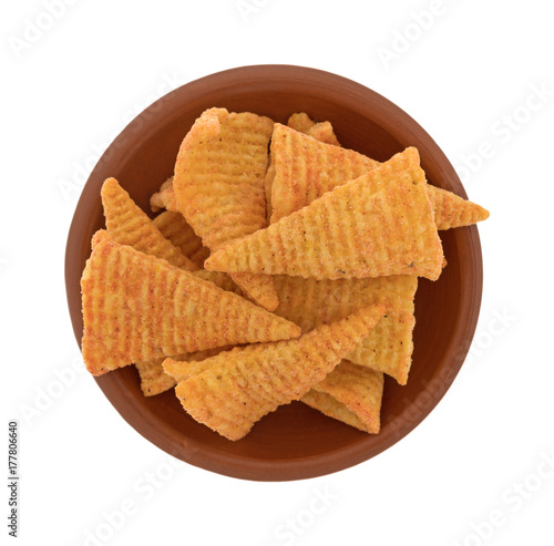 Top view of a small red clay bowl filled with cheese flavored cone shaped corn chips isolated on a white background.