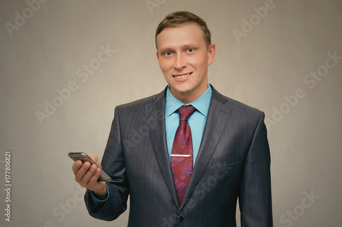 Young happy business man smiling and holding in hand mobile phone isolated. Contact us.