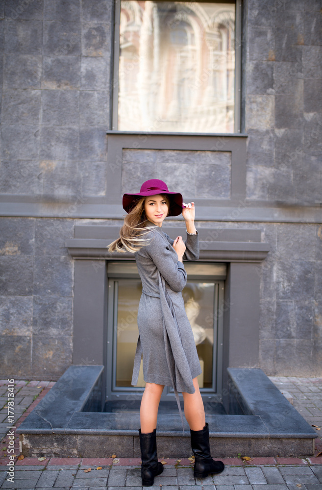 Stylish blonde model in hat wearing trendy knit dress posing at the city building Stylish blonde model in hat wearing trendy knit dress posing at the city building