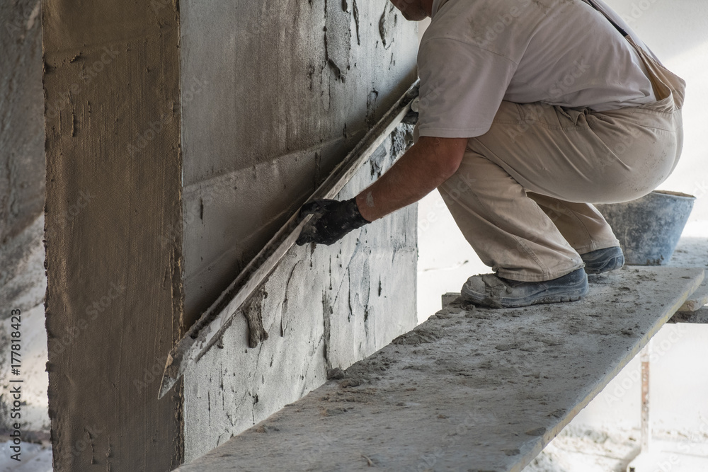 Construction worker leveling the wall surface of cement plaster Construction worker leveling the wall surface of cement plaster