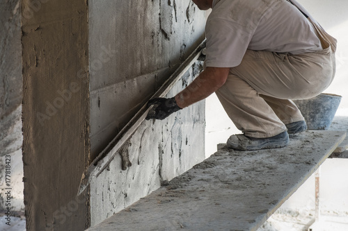 Construction worker leveling the wall surface of cement plaster © Neeqolah