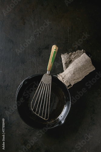 Empty oil cast-iron pan for cooking pancakes with vintage shovel over dark background. Cooking concept