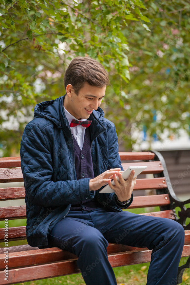 A young guy is sitting on a park bench with a phone in his hands A young guy is sitting on a park bench with a phone in his hands