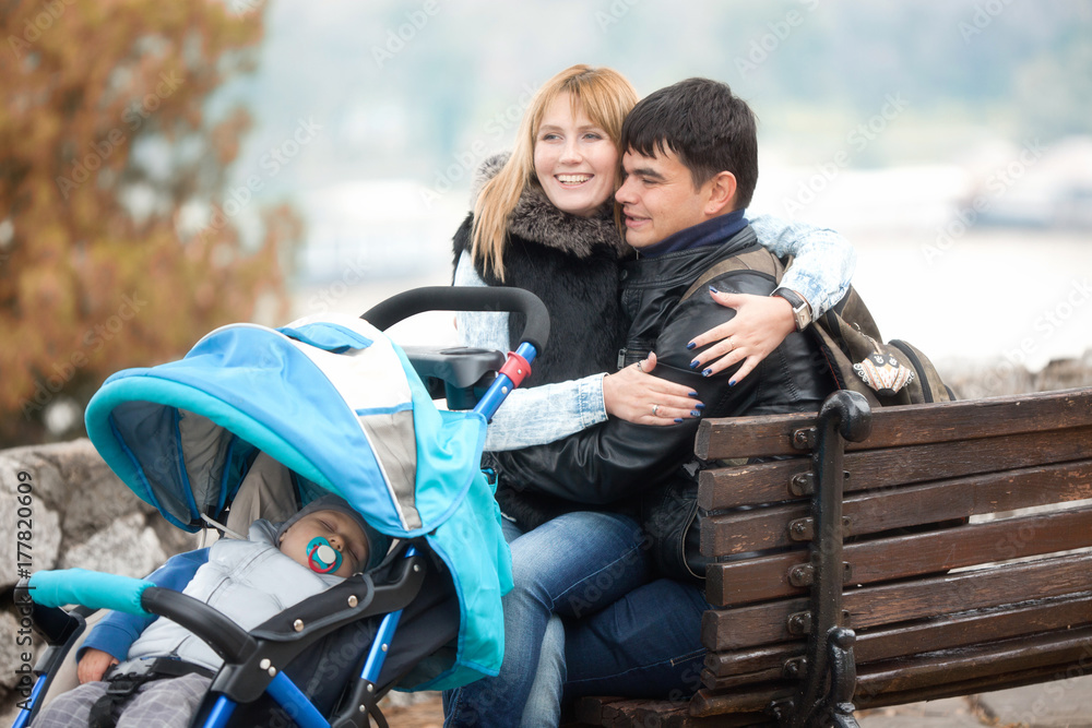 Happy Young Couple Sitting with a Little Son in  Baby Carriage