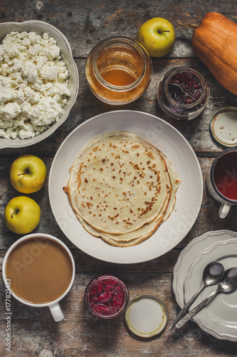 Pancakes and serving on a wooden table (honey, jam, tea, coffee, cappuccino, cocoa, cottage cheese, apples, pumpkin, etc.)