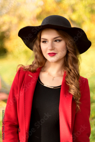 portrait of a young Halloween girl in an autumn forest in a black dress and a red coat © Tatsiana